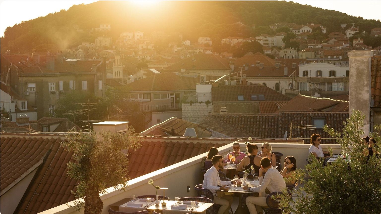 Guests chatting over drinks on a sunlit Mediterranean rooftop terrace at golden hour